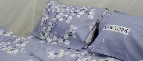 A bed with a floral-patterned bedspread and pillows, including one labeled "NEW YORK."