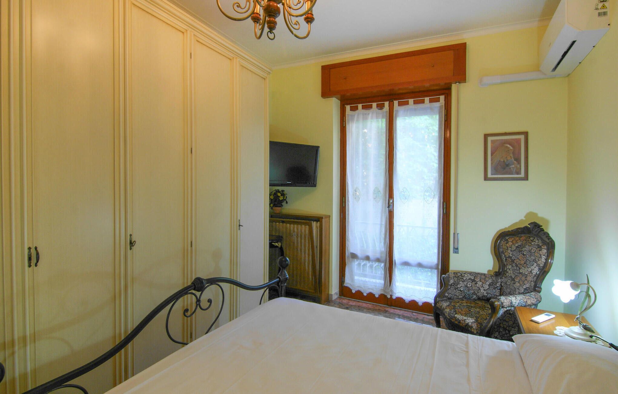 Un dormitorio con una cama, una silla, un televisor y una ventana con cortinas.