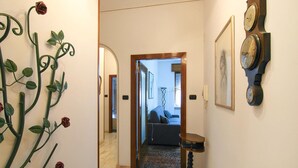 Un couloir orné d’un mur en métal décoré de motifs de roses, une porte en bois donnant sur une pièce où se trouve un canapé, et une horloge fixée au mur.