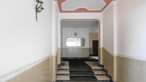 Un couloir doté d’un sol en marbre, d’un escalier recouvert d’une moquette noire et beige, d’un luminaire fixé au mur et d’un grand miroir.
