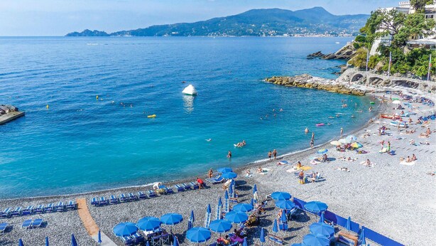 Une plage aux eaux d’un bleu limpide, bordée d’un rivage rocheux, avec une chaîne de montagnes en toile de fond.