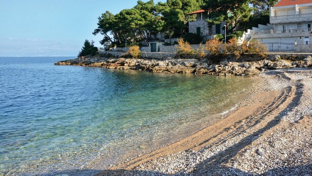 A pebble beach with clear water, a stone wall, and buildings with red roofs. - Awesome home in Stomorska with house sea view (Stomorska)