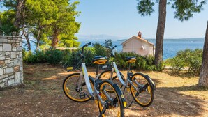 Three bicycles parked on a dirt path with a stone wall and trees, overlooking a body of water and a building with a red roof. - Awesome home in Stomorska with house sea view (Stomorska)
