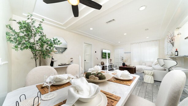 Un coin repas avec une table blanche dressée pour quatre personnes, un ventilateur de plafond et une grande plante.