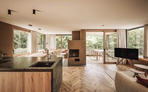 A modern kitchen with a large island, a fireplace, and a dining area with a view of the forest.