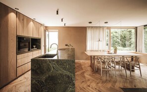 A modern kitchen with wooden cabinets, a built-in oven, and a marble island.