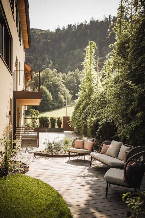 A wooden deck with outdoor seating, a staircase leading to a balcony, and a view of a forested hillside.