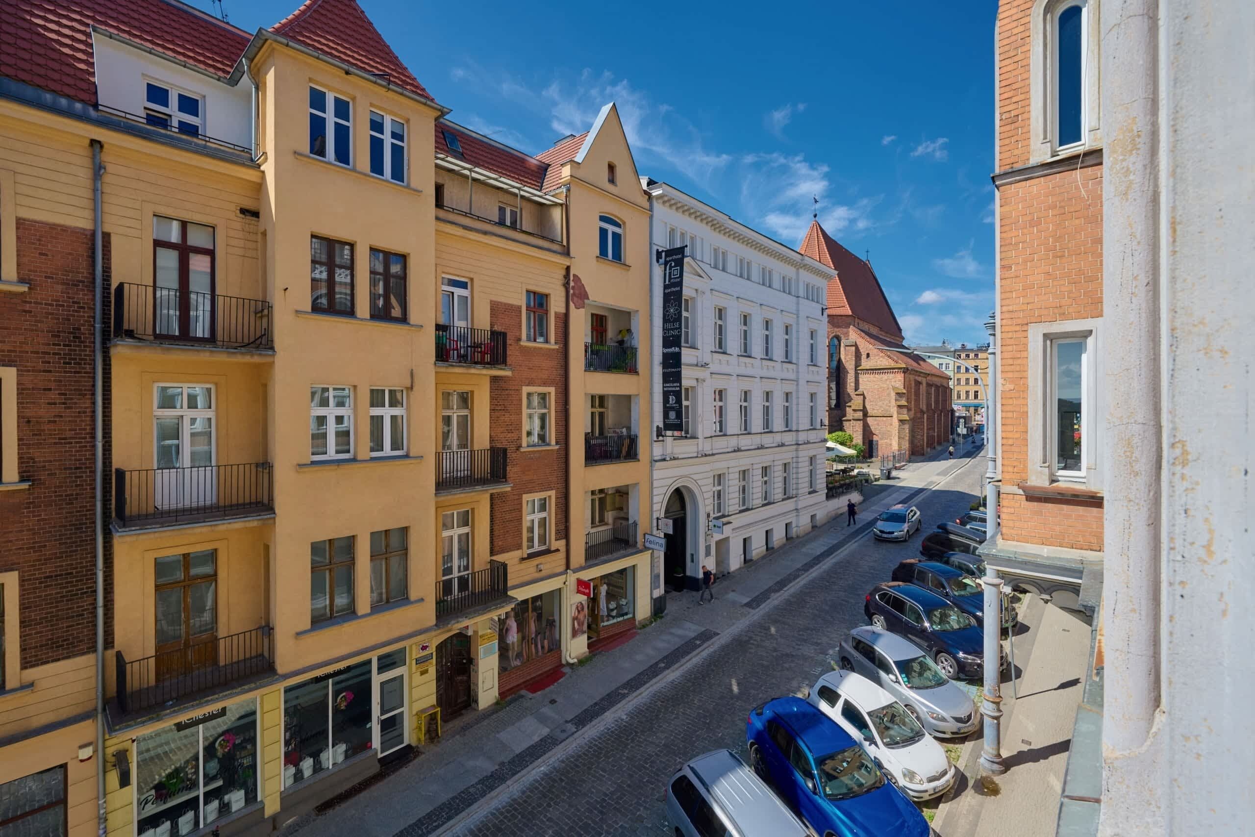 A street view with multi-story buildings, parked cars, and a clear sky.