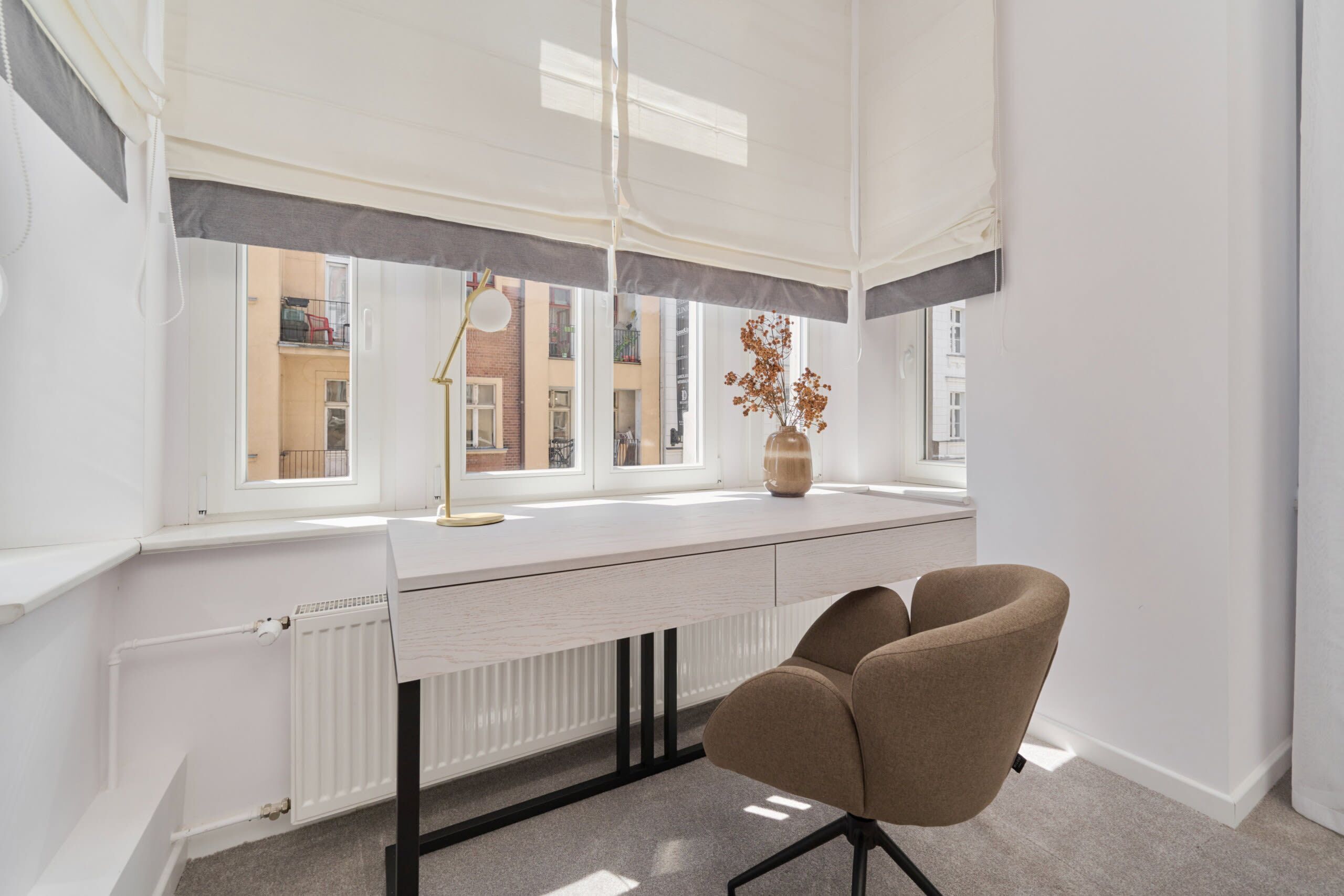 Un espacio de oficina moderno con un escritorio blanco, una silla marrón, un radiador y una ventana con vistas a edificios.