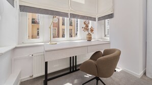 A modern office space with a white desk, a brown chair, a radiator, and a window with a view of buildings. - Elegant Apartment in Tenement House | Center, 2 Desks for Work (Poznan)