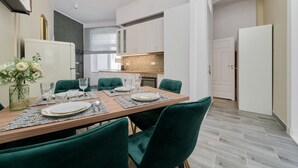 A modern dining area with a wooden table set for six, green upholstered chairs, and a vase of flowers on the left. - Elegant Apartment in Tenement House | Center, 2 Desks for Work (Poznan)