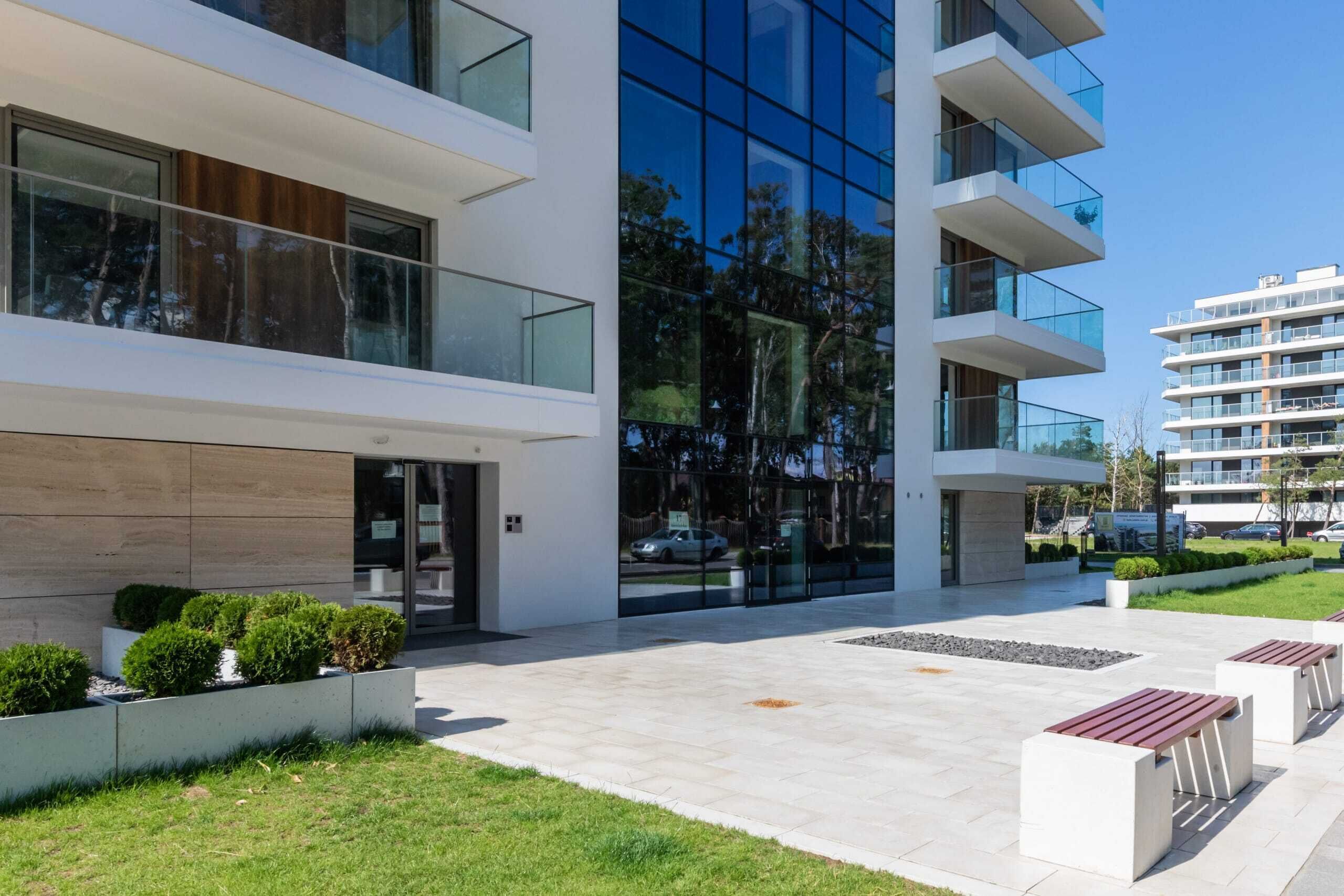 A modern building with a glass facade, outdoor seating, and a well-maintained lawn.