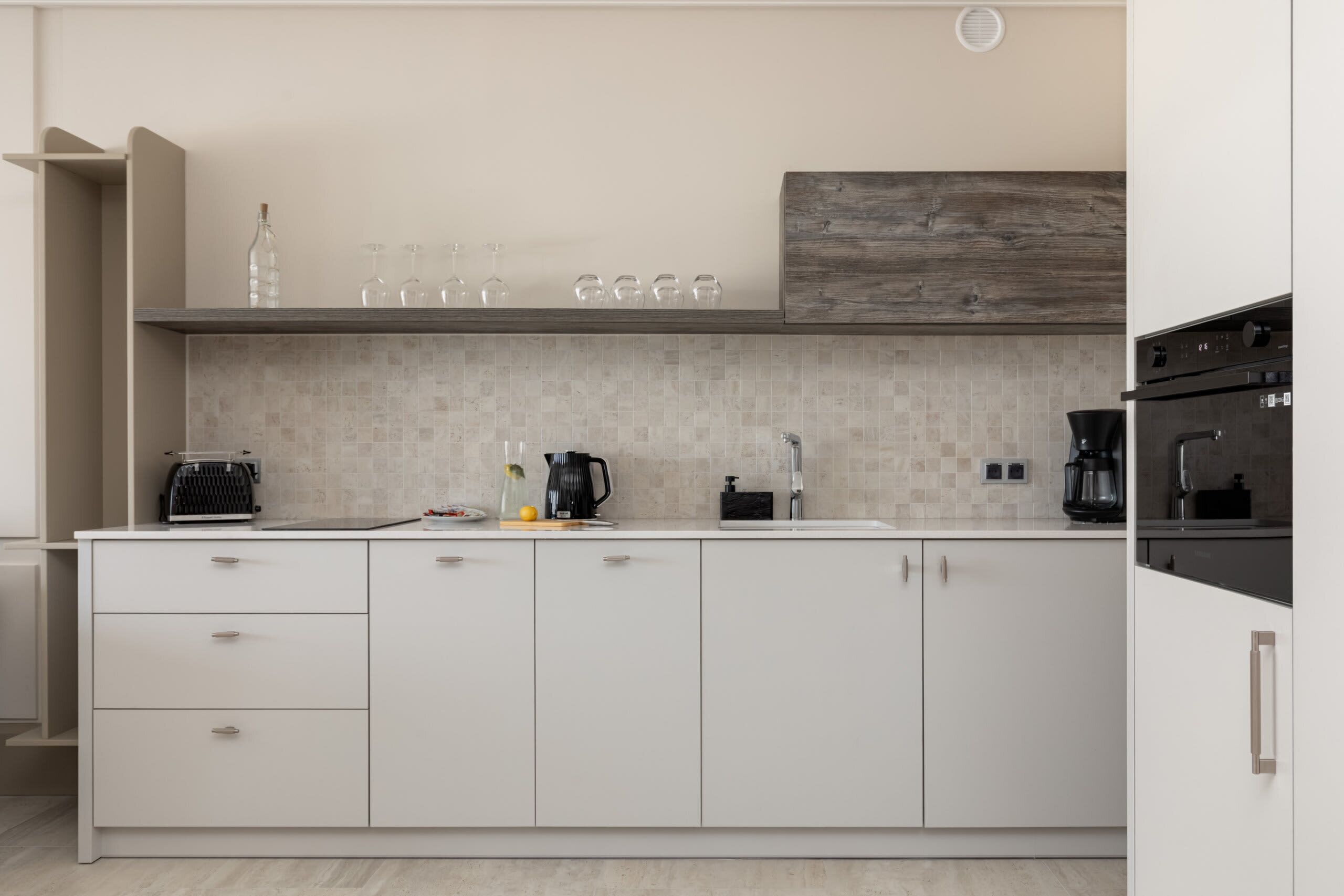 Une cuisine moderne avec des meubles blancs, un pare-feu en carrelage et un mur d’accent en bois.