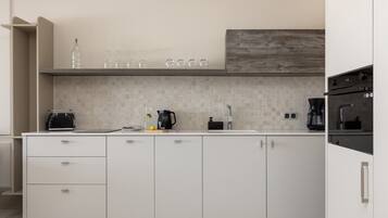Une cuisine moderne avec des meubles blancs, un pare-feu en carrelage et un mur d’accent en bois.