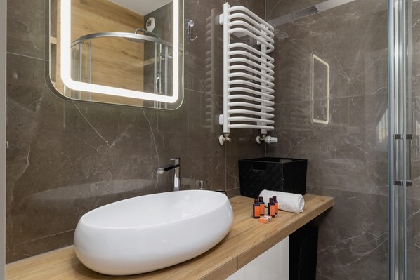 A modern bathroom with a large oval sink, a mirror with integrated lighting, a towel rack, and a shower area.