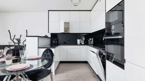 Una cocina moderna con armarios blancos, una mesa de comedor de vidrio, sillas negras y una estufa negra.