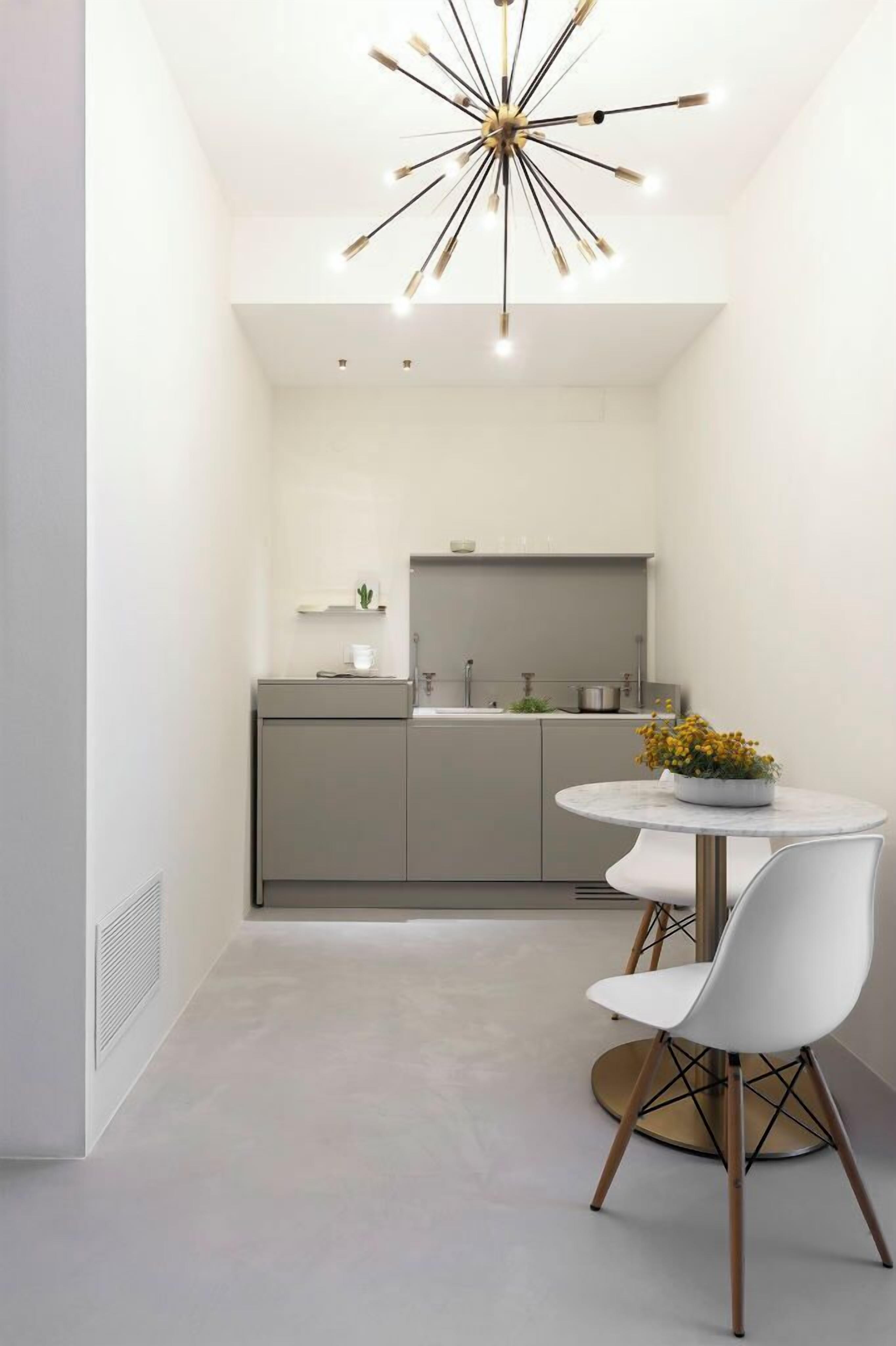 A modern kitchen with a central island, a dining area with a round table and two chairs, and a unique ceiling light fixture.