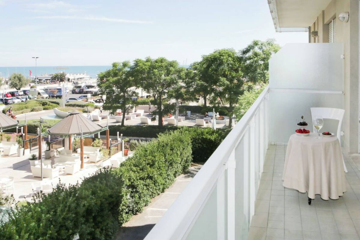 A balcony with a table set for two, overlooking a landscaped outdoor area with seating and a view of the sea.