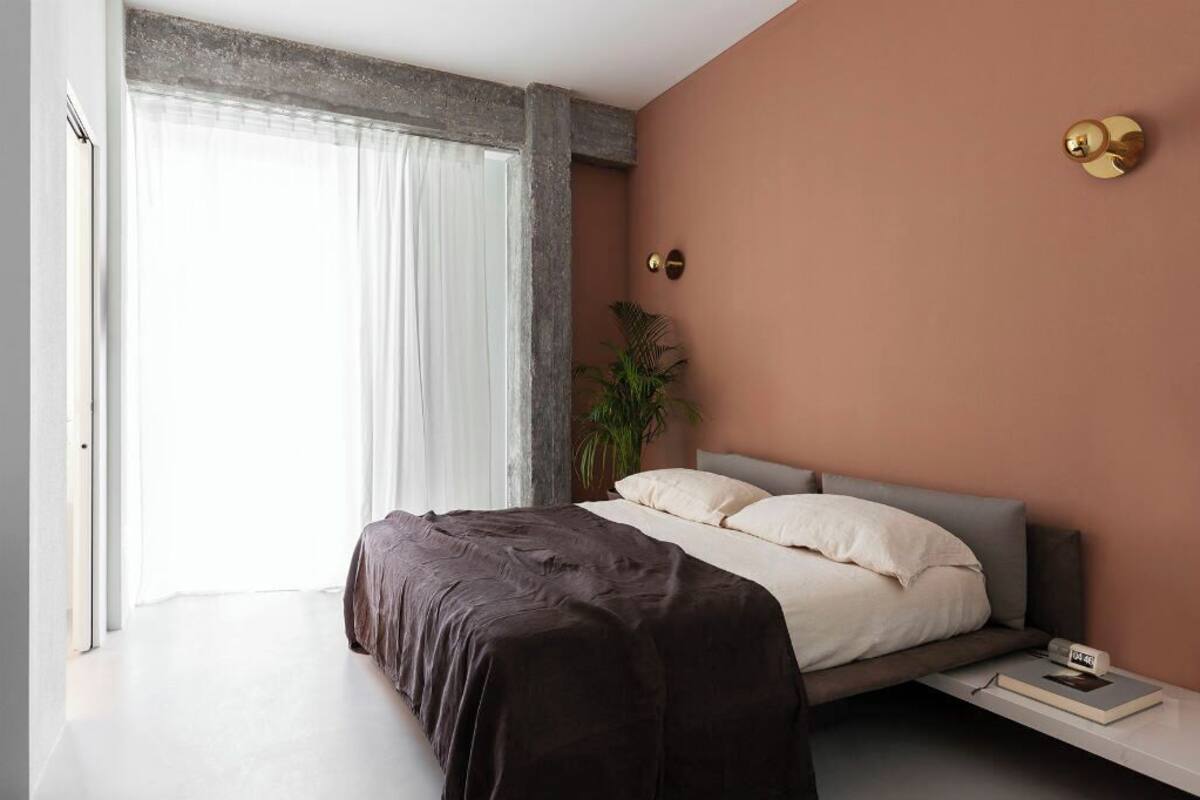 A modern bedroom with a bed, bedside table, and a window with curtains.