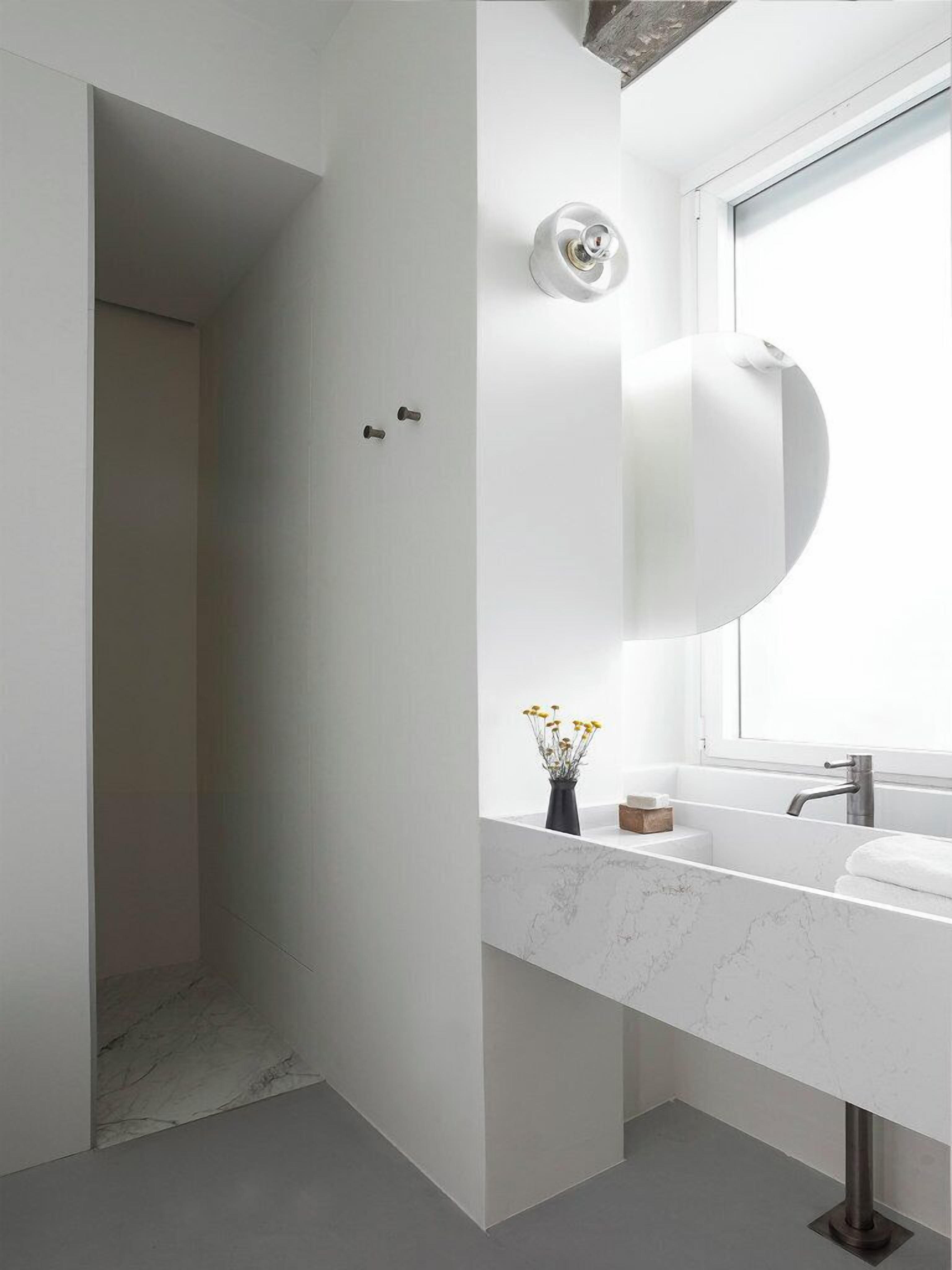 A modern bathroom with a white marble sink, a large mirror, and a window above the sink.