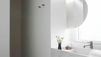 A modern bathroom with a white marble sink, a large mirror, and a window above the sink.