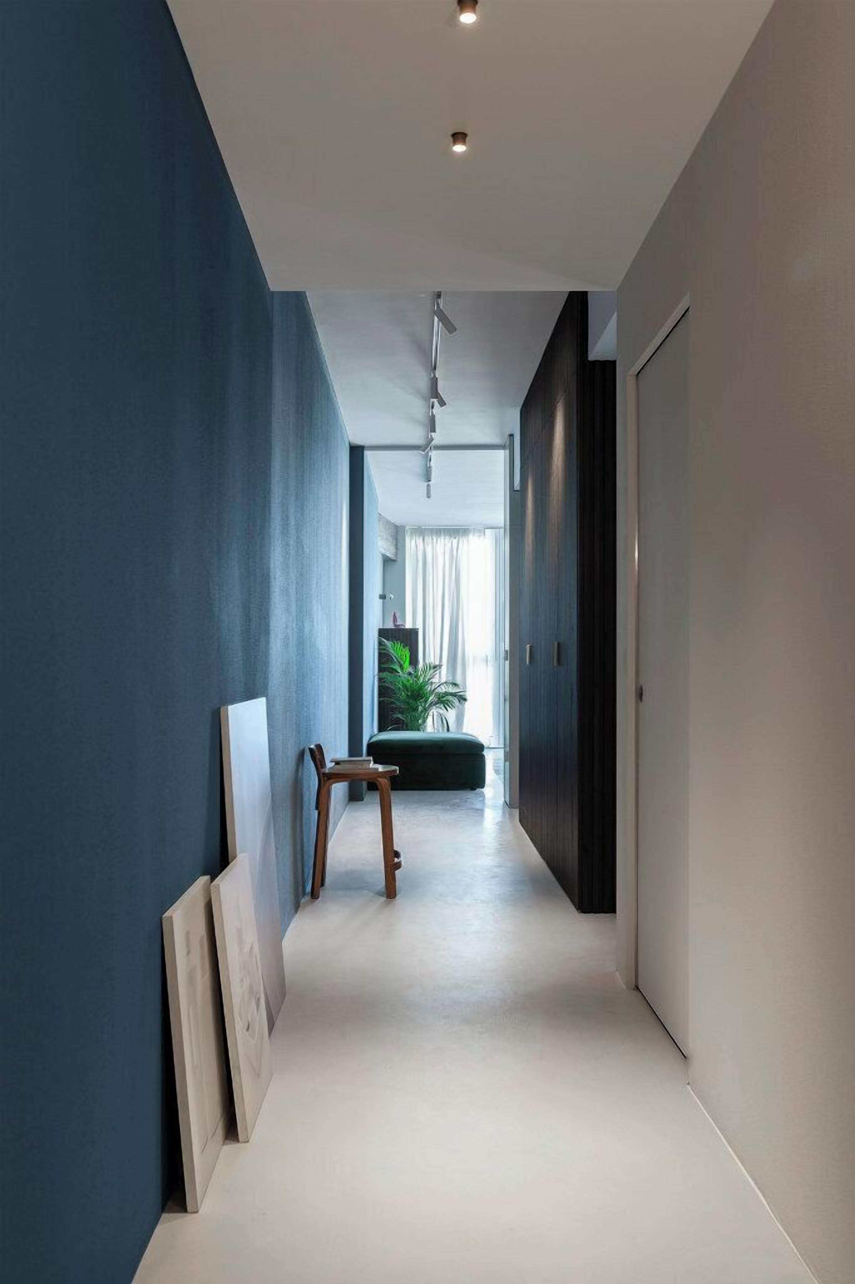 A hallway with a blue wall, a wooden chair, and a door at the end.
