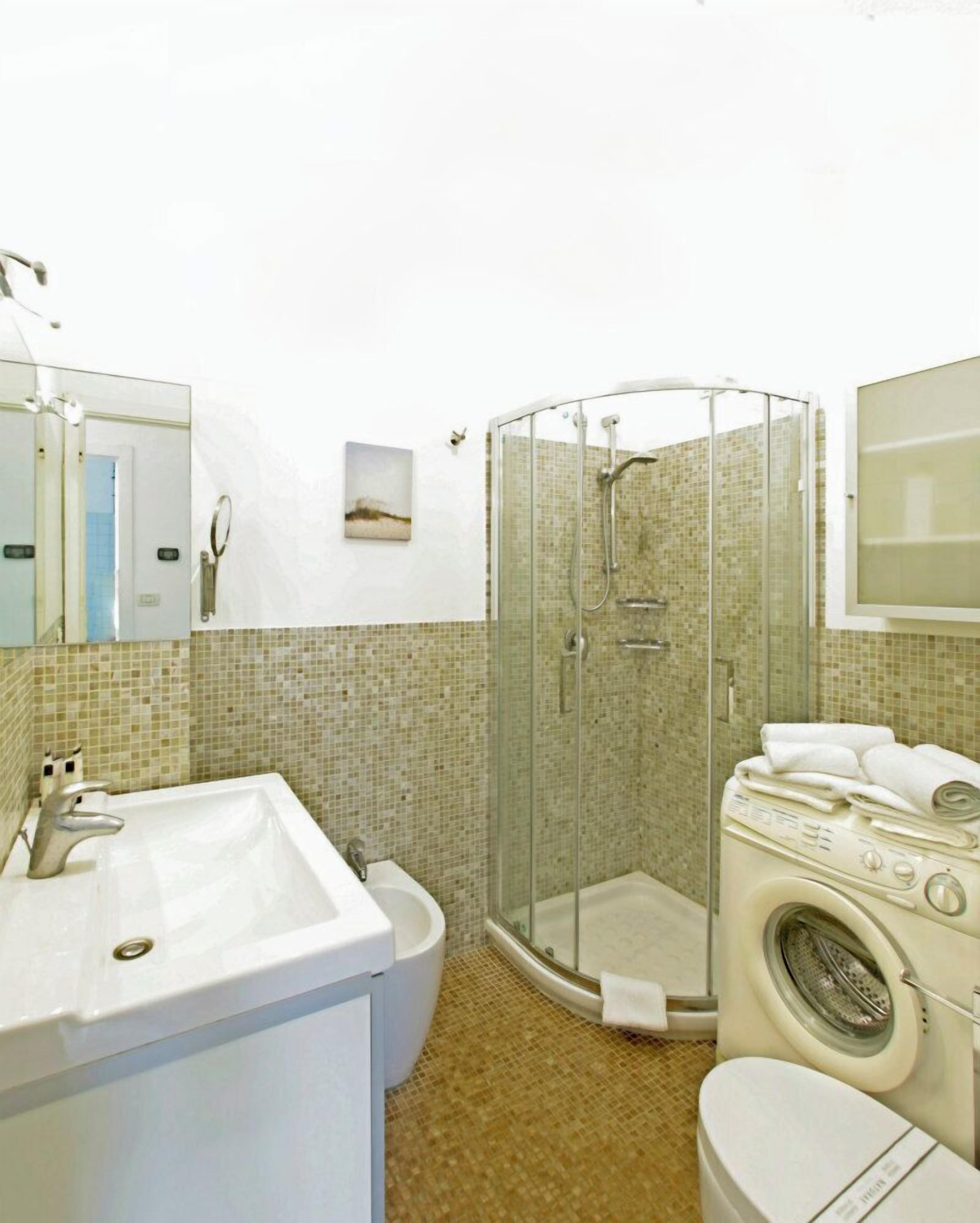 Un baño con lavamanos, inodoro, ducha y lavadora.