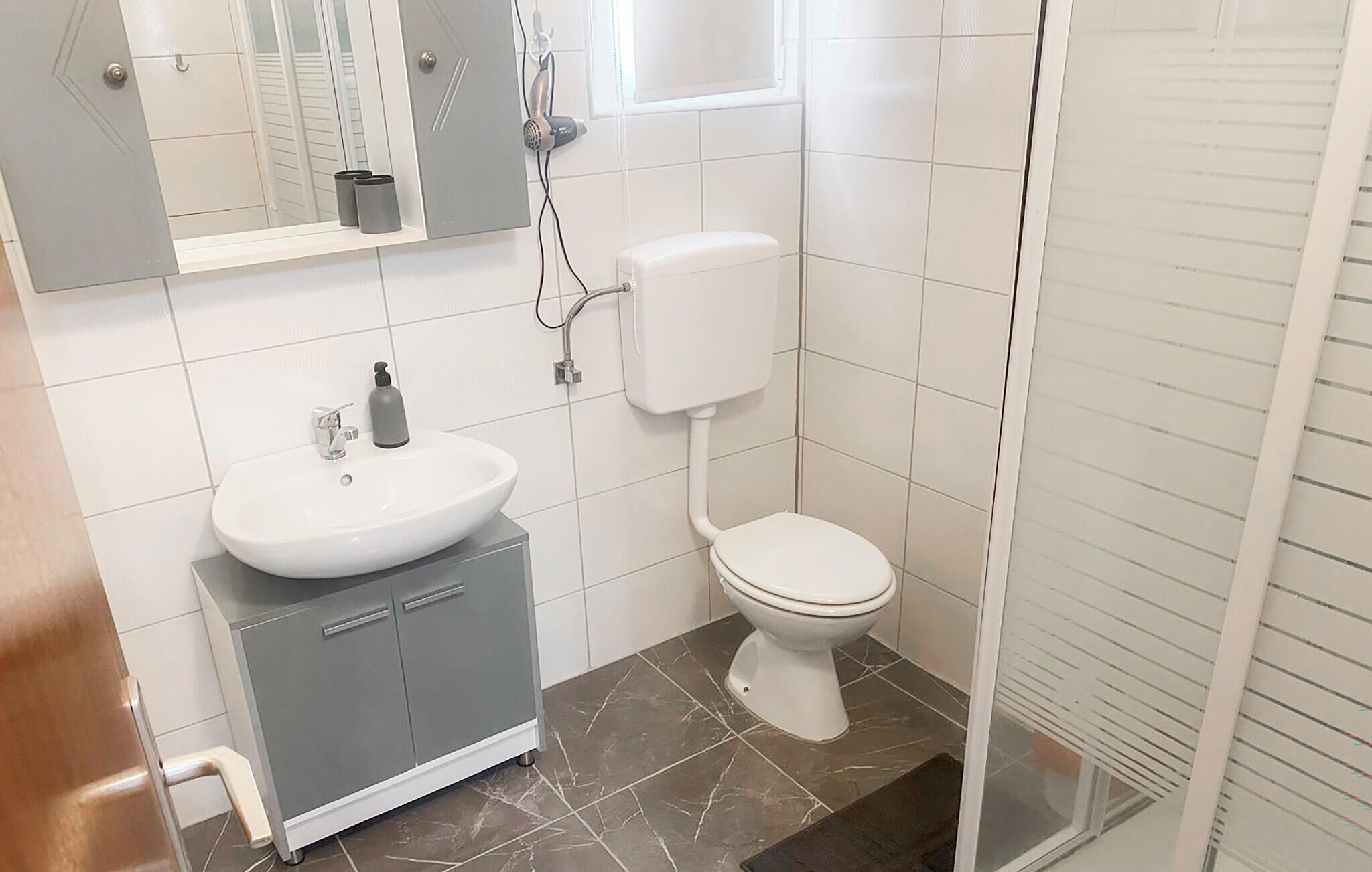 Un bagno con lavandino bianco, un water, zona doccia e un armadietto.