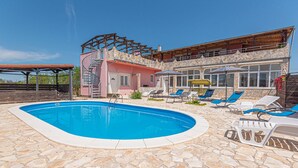 Une piscine avec des carreaux de pierre, une terrasse en bois et un bâtiment doté d’une façade en pierre et d’un balcon.
