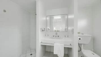 A modern bathroom with white tiles, a sink, a toilet, and a shower area.
