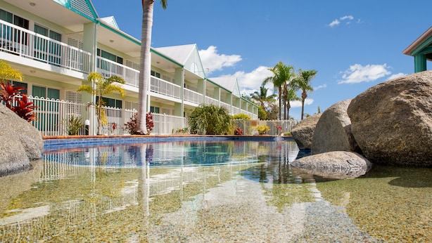 A hotel with a pool, palm trees, and large rocks. - Reef Adventureland Motel (Tannum Sands)