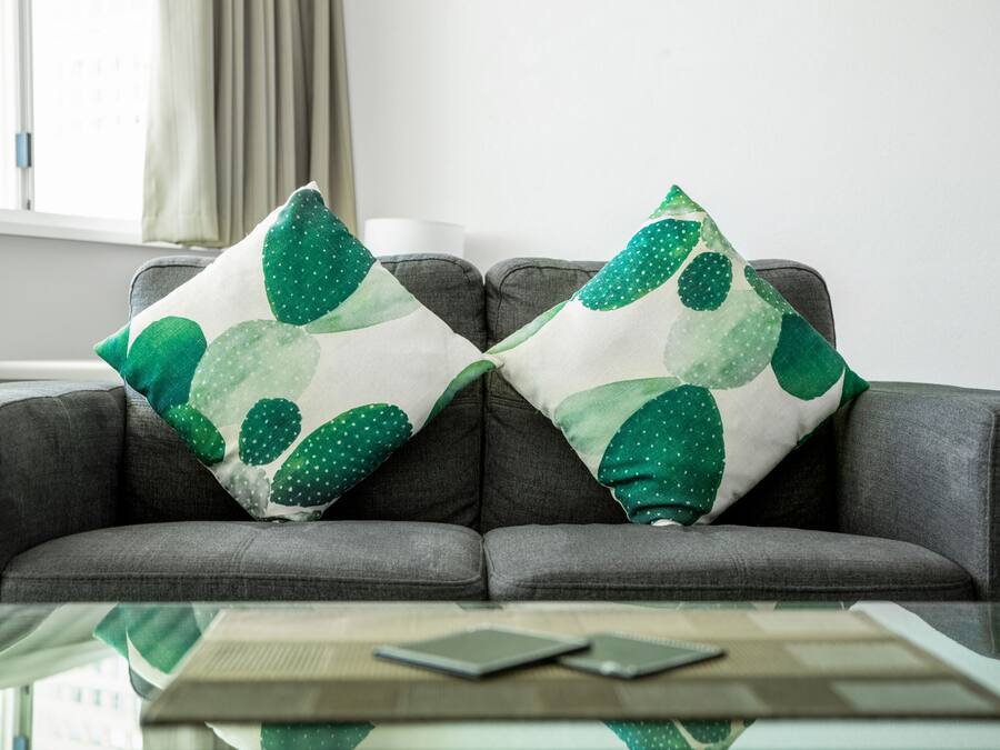 Ein graues Sofa mit zwei dekorativen Kissen mit einem grünen Blattmuster.