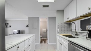 Una cocina estrecha con muebles blancos, horno empotrado y un lavamanos con grifo.
