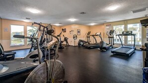 Un gimnasio con equipo de ejercicio diverso, ventanas amplias y un ventilador de techo.