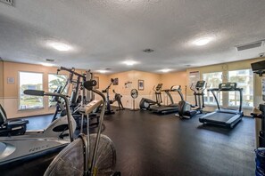 Un gimnasio con diversos equipos de ejercicio, incluyendo cintas de correr y máquinas de pesas, y amplias ventanas que ofrecen luz natural.