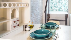 A dining area with teal plates, glasses, and a candle holder. There is a white cabinet with drawers and a window with a floral pattern. - Cozy recently renovated apartment nestled in the historic center (Savignano sul Rubicone)
