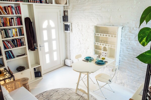 A room with a white brick wall, a bookshelf filled with books, a white table with blue plates, and a white door. - Cozy recently renovated apartment nestled in the historic center (Savignano sul Rubicone)