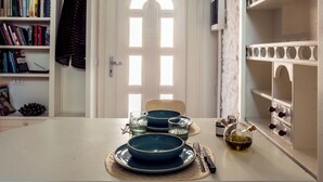 A dining area with a white table set for two, featuring blue plates and clear glasses. A wooden chair is positioned at the table, and a bookshelf filled with books is visible to the left. - Cozy recently renovated apartment nestled in the historic center (Savignano sul Rubicone)