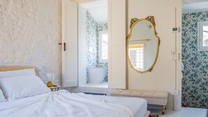 A bedroom with a bed, a bedside table, a mirror, a bathroom visible through an open door, and a patterned wall. - Cozy recently renovated apartment nestled in the historic center (Savignano sul Rubicone)