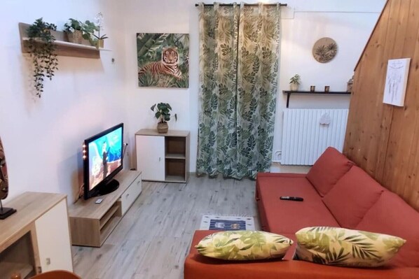 A living room with a television, a red sofa, and a plant on a shelf.