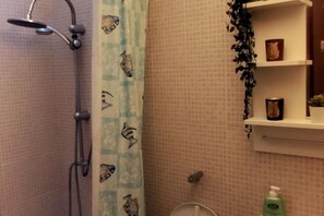 A bathroom with a shower, a toilet, a sink, and a shelf with toiletries.