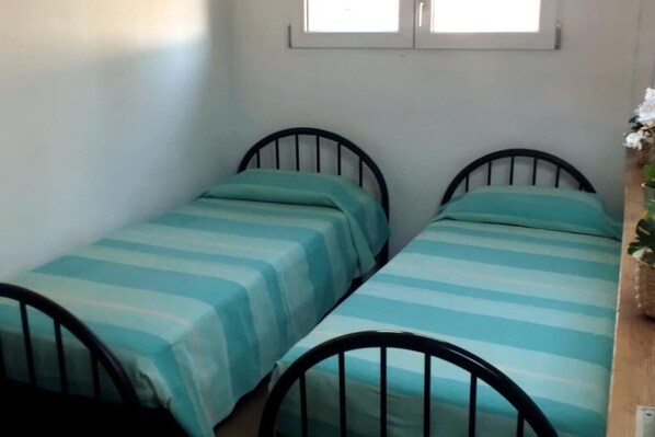A room with two single beds with metal frames, each bed has a striped bedspread.