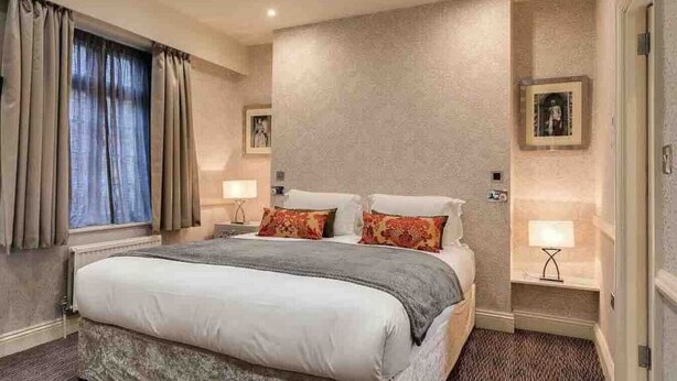 Une chambre d’hôtel avec un grand lit, deux tables de chevet avec des lampes, une fenêtre avec des rideaux et un mur à texture.
