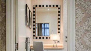 Un couloir étroit mène à une pièce où se trouvent une coiffeuse, une chaise et un grand miroir.