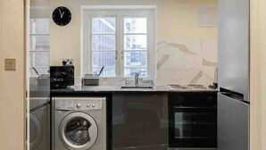 A compact kitchen with a washing machine, oven, and a clock on the wall.