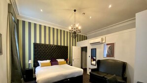 A hotel room with a large bed, a black leather sofa, a chandelier, and striped wallpaper. - 2 Bed/2 Bath Large Flat, Ground Floor, Sky TV, AC (Greater London)