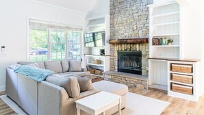 A modern living room with a stone fireplace, a sectional sofa, and a white bookshelf. - New Pool, Hot Tub, Short Walk To Beach (Union Pier)