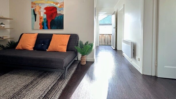 A modern living room with a sofa, a painting, a plant, and a hallway leading to a balcony.