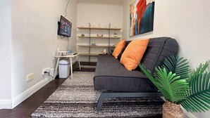 A modern living room with a sofa, a TV, a bookshelf, and a plant.