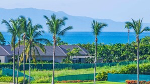 Un resort con vistas al océano y las montañas, con palmeras y un edificio de techo de tejas.